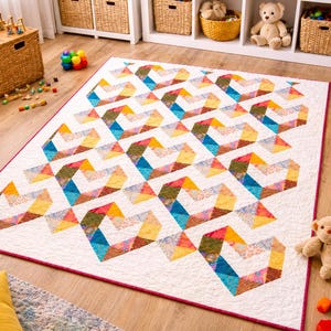 May include: A large, colorful quilt with a geometric design. The quilt features repeating shapes in shades of blue, yellow, orange, and green against a white background. The quilt is bordered with a thin red trim and is placed on a wooden floor.