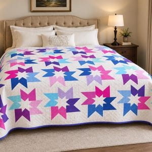 Pode incluir: Uma colcha branca com um padrão de estrelas repetitivo em tons de rosa choque, roxo, azul claro e azul escuro. A colcha apresenta um design geométrico limpo com formas de estrelas pontiagudas dispostas numa grelha sobre a superfície.