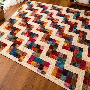 May include: A colorful, rectangular quilt with a zig-zag pattern. The quilt features a cream-colored background with vibrant blocks of red, blue, yellow, and green. The quilt is likely made of fabric and is suitable for a bed or floor.