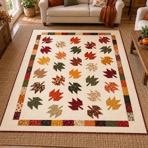 May include: A rectangular quilt featuring a cream-colored background decorated with a repeating pattern of fabric maple leaves in shades of red, orange, yellow, brown, and green. The border consists of small, multicolored fabric squares.