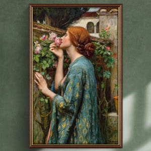 Könnte beinhalten: Gerahmtes Gemälde einer rothaarigen Frau, die an einer rosa Rose riecht. Sie trägt eine türkisfarbene Robe mit goldenem Muster. Der Hintergrund zeigt einen Rosengarten und ein Gebäude mit Bogenfenstern. Das Kunstwerk ist in einem Holzrahmen.