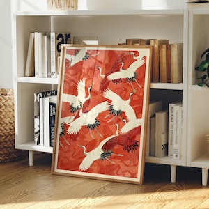 May include: A framed rectangular art print featuring a pattern of white cranes with red and black wing details flying against a textured, vibrant red background. The artwork is displayed in a light-toned wooden frame, showcasing multiple birds in various flight positions across the composition.