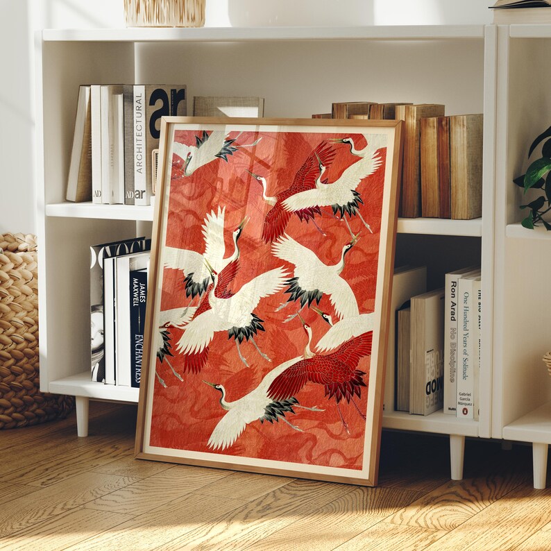 May include: A framed rectangular art print featuring a pattern of white cranes with red and black wing details flying against a textured, vibrant red background. The artwork is displayed in a light-toned wooden frame, showcasing multiple birds in various flight positions across the composition.