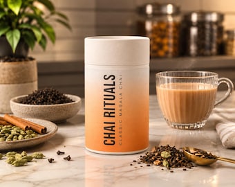 Puede incluir: Un recipiente cilíndrico con degradado blanco y naranja etiquetado como CHAI RITUALS CLASSIC MASALA CHAI. Está rodeado de hojas de té sueltas, vainas de cardamomo verde, ramas de canela y una taza de cristal con una bebida de té marrón.