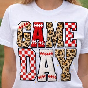 May include: White t-shirt with the words "GAME DAY" in a baseball-themed design. The letters have a mix of patterns, including leopard print, red with white stitching, and a red and white checkered pattern. The shirt also has the text "HIGH QUALITY 300 DPI" and "PNG+PDF".