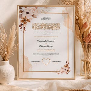 May include: A framed marriage certificate with floral accents in shades of pink and brown. The certificate includes the names Naveed Ahmed and Kiran Tariq, with Arabic script at the top. The frame is gold.