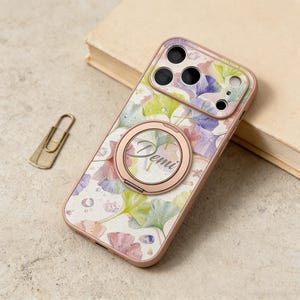 May include: A floral phone case with a rose gold ring holder. The case features a watercolor design with green, purple, and pink leaves on a white background. The name "Demi" is printed on the ring holder.