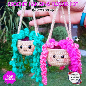 May include: Two crochet hanging flower pots with smiling faces, one with teal trailing foliage and one with bright pink trailing foliage. Each pot is beige with black eyes and pink cheeks, suspended by tan yarn cords. Text reads CROCHET HANGING FLOWER POT.