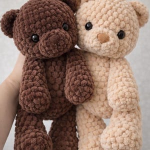 May include: Two plush teddy bears made of thick, textured yarn. One bear is dark brown and the other is light beige. Both have round ears, dark plastic eyes, and a small stitched nose. The beige bear features a small white pom-pom on its head.