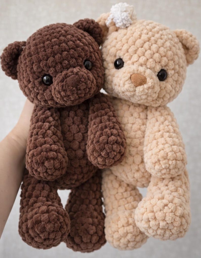 May include: Two plush teddy bears made of thick, textured yarn. One bear is dark brown and the other is light beige. Both have round ears, dark plastic eyes, and a small stitched nose. The beige bear features a small white pom-pom on its head.