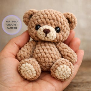 May include: A miniature crocheted teddy bear in brown and beige tones. The bear features black eyes and a brown nose. The text "MINI BEAR CROCHET PATTERN" is in a purple circle. This handmade bear is a charming example of crochet craftsmanship.