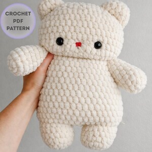 May include: A cream-colored, handmade crochet bear with black button eyes and a small red nose. The bear has a textured, plush appearance and is holding its arms out. The image includes a circular graphic that says "CROCHET PDF PATTERN".