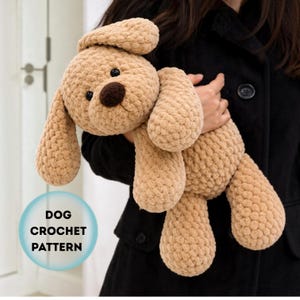 Op de afbeelding: Een beige gehaakte hondenknuffel met een donkerbruine neus en zwarte ogen. Het speelgoed heeft een getextureerde, zachte garenconstructie met lange slappe oren. Een blauwe cirkelvormige afbeelding bevat de tekst DOG CROCHET PATTERN.