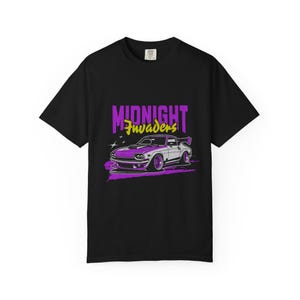 May include: Black t-shirt featuring a graphic of a purple and white muscle car with a spoiler. The text "MIDNIGHT INVADERS" is above the car in purple and yellow. The design includes stars and a stylized background.