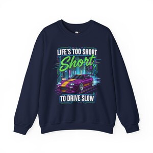 May include: Dark blue sweatshirt featuring a purple sports car with yellow detailing, racing through a city at night. The text "LIFE'S TOO SHORT TO DRIVE SLOW" is above the car.