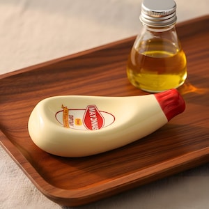 Puede incluir: Una bandeja de madera con una pequeña fuente en forma de mayonesa y una pequeña botella de vidrio. La fuente es de color blanquecino con un extremo rojo y lleva la inscripción "Mayonnaise".