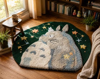 May include: A circular tufted rug featuring a large, grey, furry creature with pointed ears and a white belly with grey chevron markings. The rug has a dark green background decorated with small, embroidered yellow and orange stars and constellations.