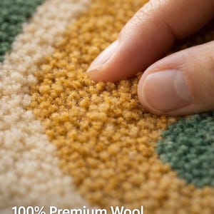 Close-up of premium wool rug fibers showing dense hand tufted texture, soft plush surface with green and mustard yarn detail, hand touching rug