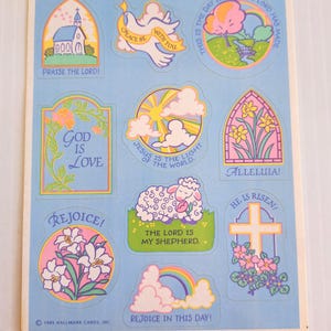 Puede incluir: Una hoja de pegatinas Hallmark vintage con temas religiosos. Los diseños incluyen una iglesia, una paloma, un arcoíris, un cordero y arreglos florales. El texto incluye "Praise the Lord!", "God is Love" y "Rejoice!"