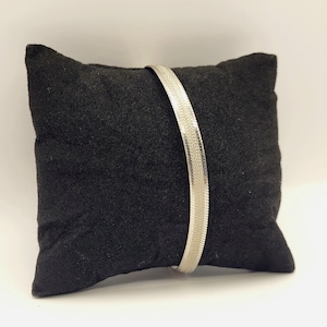 Op de afbeelding: Een zilverkleurige armband met visgraatketting, voorzien van een plat, flexibel ontwerp met een gepolijst, reflecterend oppervlak. De armband wordt in een gebogen, verticale positie getoond, wat het ingewikkelde, in elkaar grijpende V-patroon benadrukt.