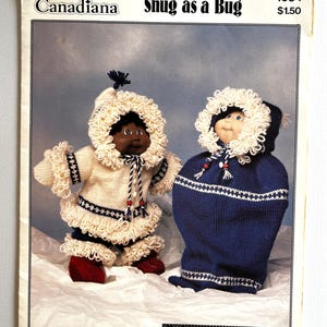 Könnte beinhalten: Ein Vintage-Strickmusterheft mit dem Titel Patons Canadiana Snug as a Bug 1034. Das Cover zeigt zwei Puppen in gestrickten Winteroutfits: eine in einem weißen Parka mit weißem Besatz und roten Stiefeln und eine in einem blauen Kapuzen-Schlafsack.