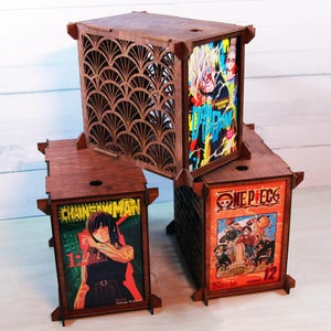 May include: Three wooden anime-themed display boxes. The largest box has a decorative fan-shaped cutout. The other two boxes feature manga covers from "Chainsaw Man" and "One Piece". The boxes are stained a dark brown color.