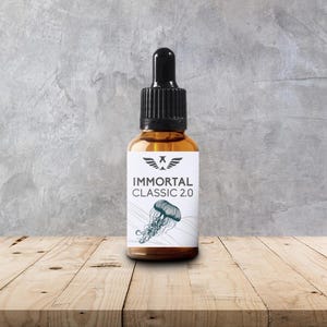 May include: A brown glass bottle with a black dropper top. The label reads "IMMORTAL CLASSIC 2.0" with a jellyfish illustration. The bottle sits on a wooden surface against a gray concrete wall.