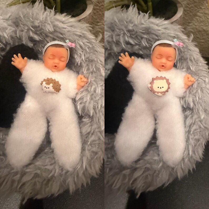 May include: A doll dressed in a white, fluffy outfit with a hedgehog applique, lying on a gray, furry surface. The doll has a white headband with a pink bow and is posed with arms outstretched. The doll's skin is a light peach color.