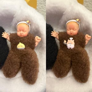May include: A small doll dressed in a brown fuzzy outfit with outstretched arms. The doll has a white headband with a small decoration and a small pin on the chest. The doll is lying on a white surface.