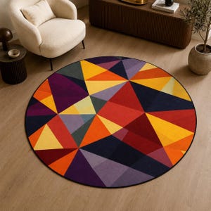May include: A circular area rug featuring a geometric pattern of triangles in vibrant shades of red, orange, yellow, purple, and dark blue. The rug has a black border and is laid flat on a light-colored wooden floor surface.