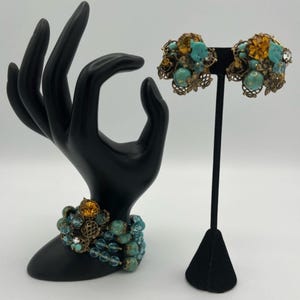 Könnte beinhalten: Vintage Schmuckset mit Armband und Clip-Ohrringen. Das Armband hat mehrere Stränge aus türkisfarbenen und klaren Perlen, akzentuiert mit bernsteinfarbenen Steinen und filigranen Metallarbeiten. Die Ohrringe spiegeln das Design mit türkisfarbenen und bernsteinfarbenen Steinen wider.