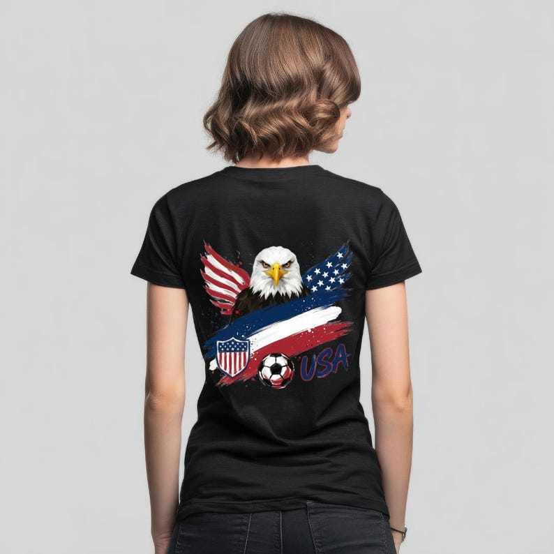 May include: Black t-shirt featuring a patriotic design. The graphic includes a bald eagle, the American flag, a soccer ball, and the word "USA". The design incorporates red, white, and blue colors, creating a bold and eye-catching look.