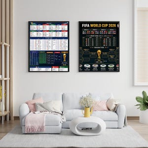 May include: Two framed posters with black borders hang on a white wall. The poster on the right displays "FIFA WORLD CUP 2026" and a tournament bracket. The left poster shows a schedule. A white couch and coffee table are in front.