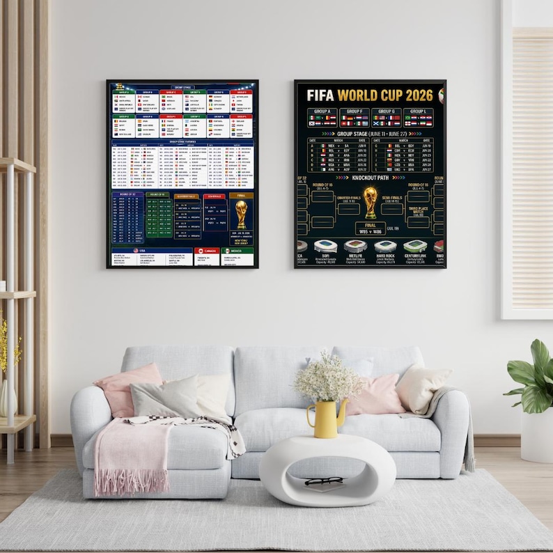 May include: Two framed posters with black borders hang on a white wall. The poster on the right displays "FIFA WORLD CUP 2026" and a tournament bracket. The left poster shows a schedule. A white couch and coffee table are in front.