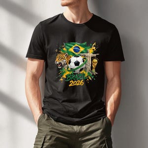 May include: Black t-shirt featuring a soccer ball, the Brazilian flag, the Christ the Redeemer statue, and a jaguar. The shirt also includes the text "BRAZIL 2026" in yellow and green, with a gold trophy.