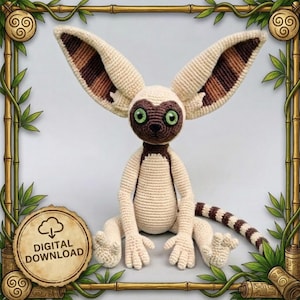 May include: A crocheted stuffed animal featuring a cream-colored body, large pointed ears with brown and tan striped patterns, and bright green eyes. The creature has a dark brown face mask, a long striped tail, and a digital download icon in the corner.