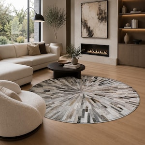 May include: A circular area rug featuring a radial pattern of rectangular patches in shades of gray, white, brown, and black. The rug is composed of numerous thin, elongated segments arranged in a sunburst design, creating a textured surface.