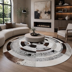 May include: A large circular area rug featuring a patchwork design of cowhide in shades of brown, white, grey, and black. The rug is composed of concentric rings of varying textures and patterns, creating a geometric radial effect on the floor.
