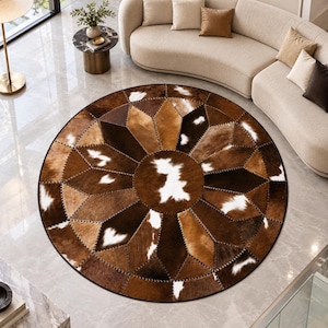 May include: A circular area rug constructed from stitched panels of cowhide in various shades of brown, tan, and white. The rug features a geometric starburst pattern radiating from a central circular patch, with visible dark stitching along edges.