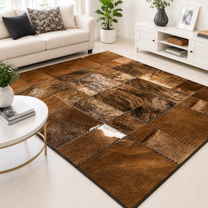 May include: A rectangular area rug constructed from stitched square patches of cowhide in various shades of brown, tan, and dark chocolate, featuring natural hair textures and a single small patch of white fur near the center of the rug.