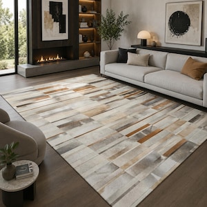 May include: A rectangular area rug featuring a geometric pattern of stitched leather panels in shades of cream, beige, tan, brown, and gray. The rug displays a linear, multi-tonal design with varying rectangular shapes arranged in a repeating horizontal layout.