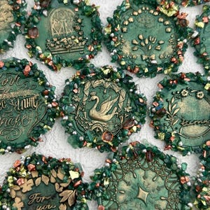 Peut inclure: Une collection de pièces décoratives circulaires vertes avec divers motifs et textes. Chaque pièce présente une image ou une inscription centrale, entourée d'une bordure d'accents verts, dorés et irisés. Les motifs incluent un cygne, des compositions florales et des inscriptions.
