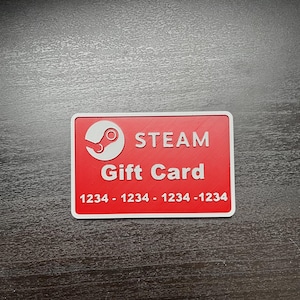 Puede incluir: Una tarjeta de regalo Steam roja con texto blanco y un logotipo de Steam. La tarjeta tiene un borde blanco y una serie de números en la parte inferior. La tarjeta es rectangular y está sobre una superficie de madera oscura.