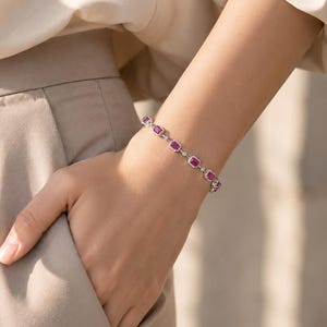 May include: A silver-toned bracelet featuring a series of rectangular, deep pink gemstones, each surrounded by a halo of small, clear, sparkling stones. The links are connected by small, round, clear stones, creating a delicate, continuous chain.