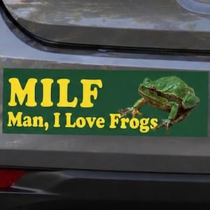 May include: Green bumper sticker with yellow text that reads "MILF Man, I Love Frogs." A green frog is pictured on the right side of the sticker. The sticker is affixed to the back of a vehicle.