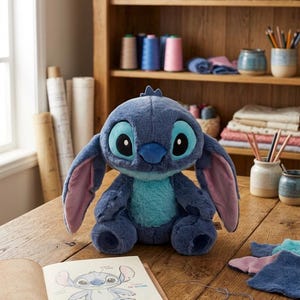 May include: A blue Stitch soft toy with big eyes and ears, placed on a wooden table. An open sketchbook with a Stitch drawing is in front of the toy. The background features sewing supplies and a wooden shelf.