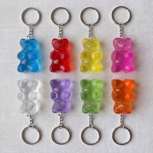 May include: Eight colorful gummy bear keychains. Each bear is a different color: blue, red, yellow, pink, clear, purple, green, and orange. The keychains have silver-colored rings.