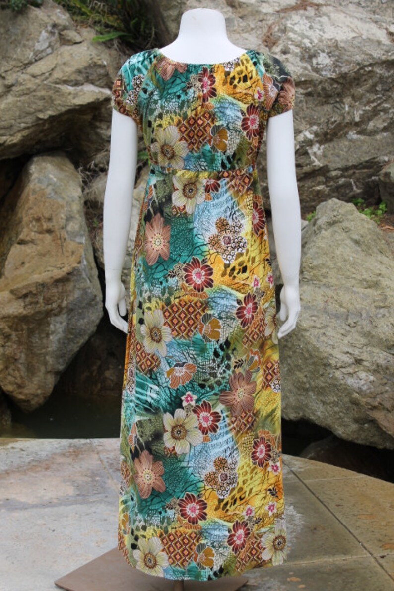 May include: A long, flowing maxi dress with a colorful floral print. The dress has a scoop neck, short sleeves, and a fitted bodice. The print features a variety of flowers, leaves, and geometric patterns in shades of yellow, green, blue, brown, and red.