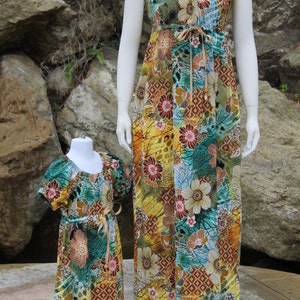 May include: Two matching dresses with a colorful floral print in shades of blue, green, yellow, and brown. The dresses have a scoop neckline, short sleeves, and a tie at the waist.