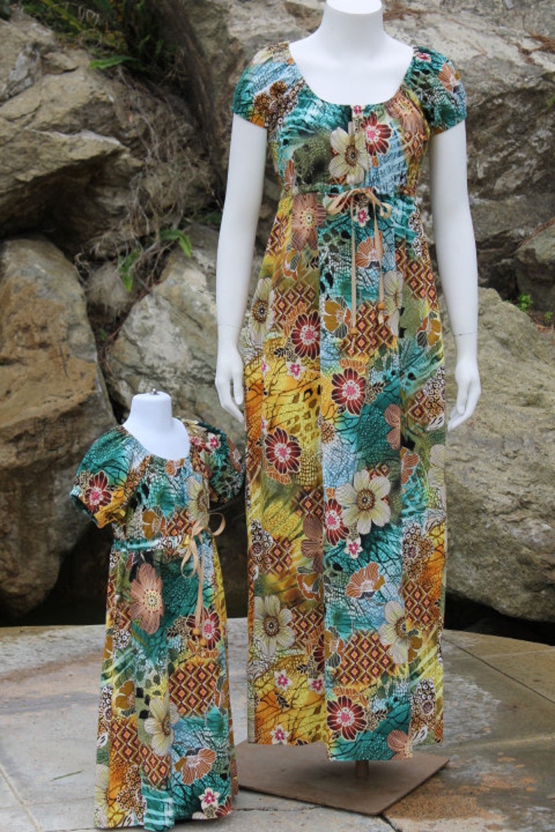 May include: Two matching dresses with a colorful floral print in shades of blue, green, yellow, and brown. The dresses have a scoop neckline, short sleeves, and a tie at the waist.